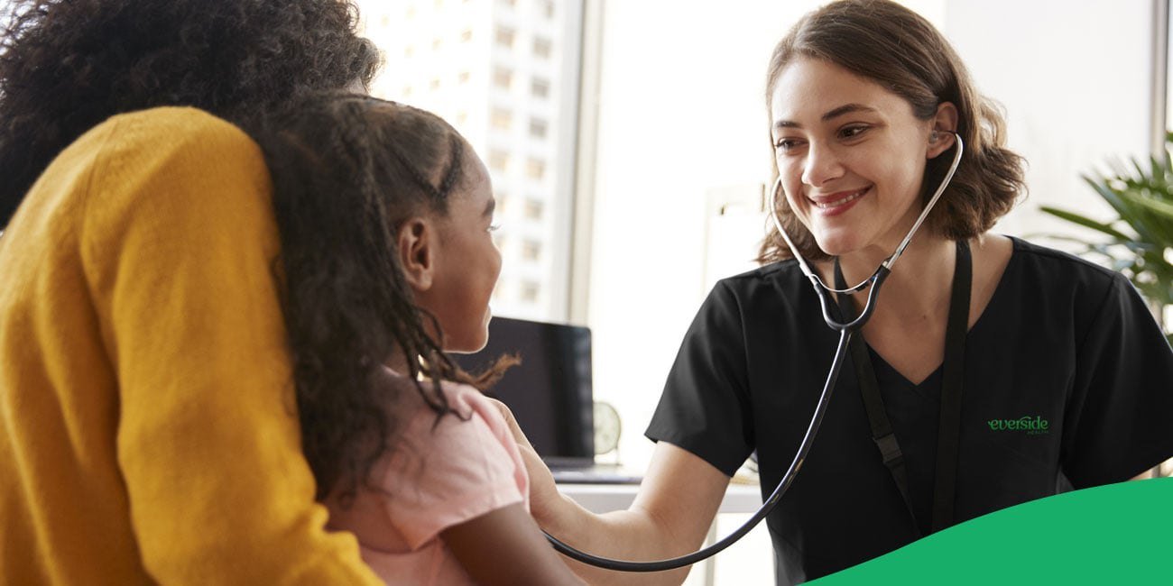 nurse smiling while checking child heartbeat with stethoscope